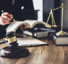 Man writing on a book with books, justice scale and court gravel on a table.