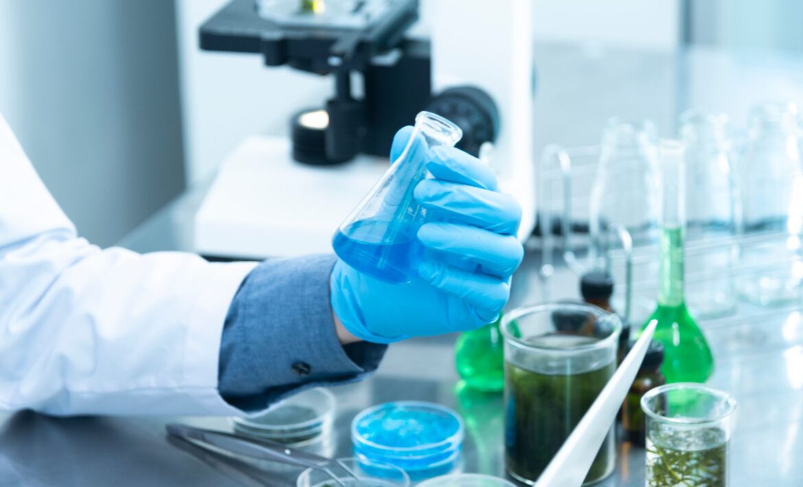 Man with blue glove holding a tube with blue liquid in lab.