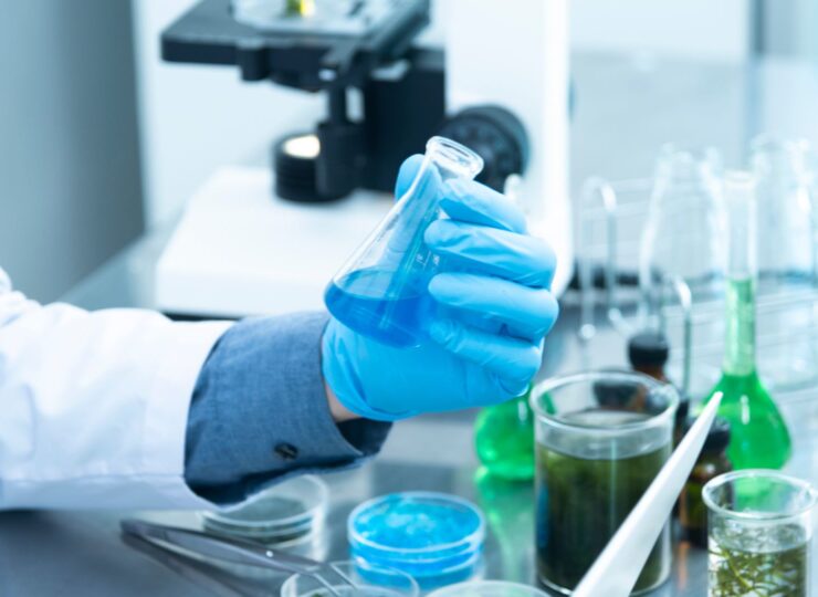 Man with blue glove holding a tube with blue liquid in lab.