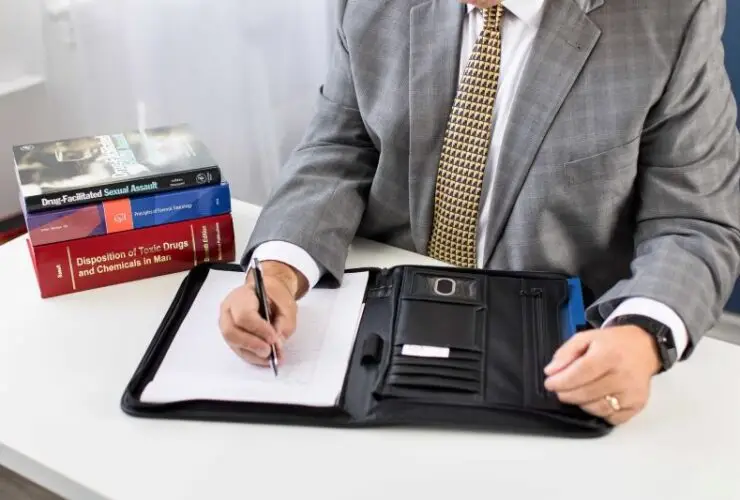 Marc LeBeau writing on a book with a pen on the desk with books on the table.