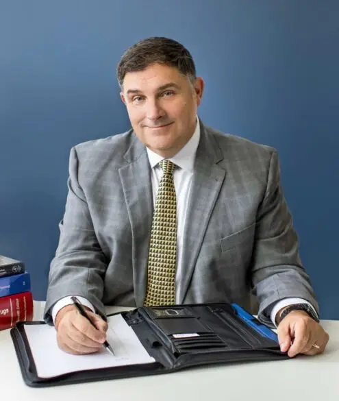 Marc LeBeau sitting on the desk facing camera while writing on a book with a pen.