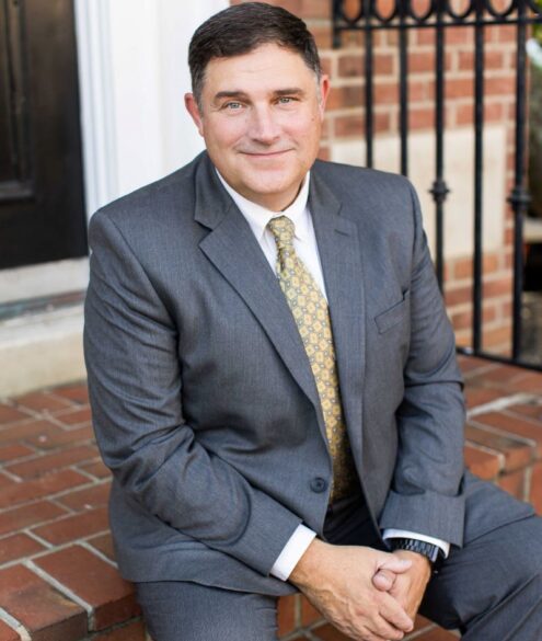 Dr. Marc LeBeau sitting on the stairs wearing grey suit, smiling to the camera.